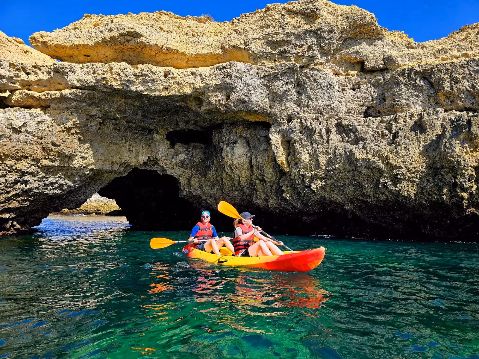 Couple kayaking in crystal clear green waters beside stunning Albufeira rocky sea caves and natural arches