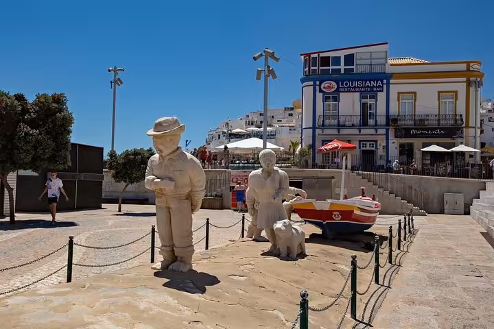 Statues and a colorful boat adorn a charming square in Albufeira, ideal for a cultural city walk with a local guide.