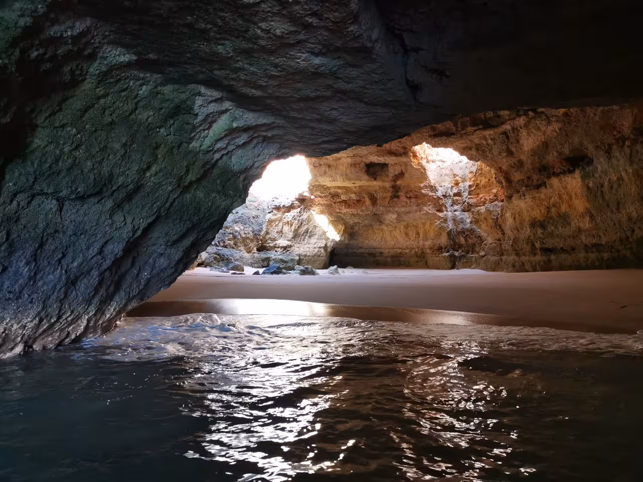 Inside an Algarve sea cave with sandy beach and sunlight, explored on a private Albufeira boat charter cruise