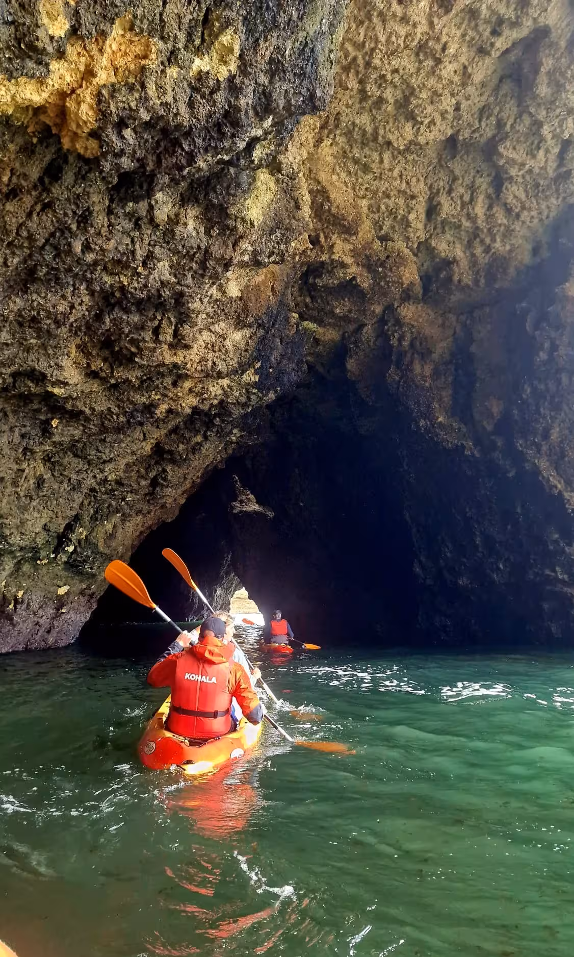Group of kayakers entering a dramatic dark sea cave on an Albufeira guided kayak tour in Algarve Portugal