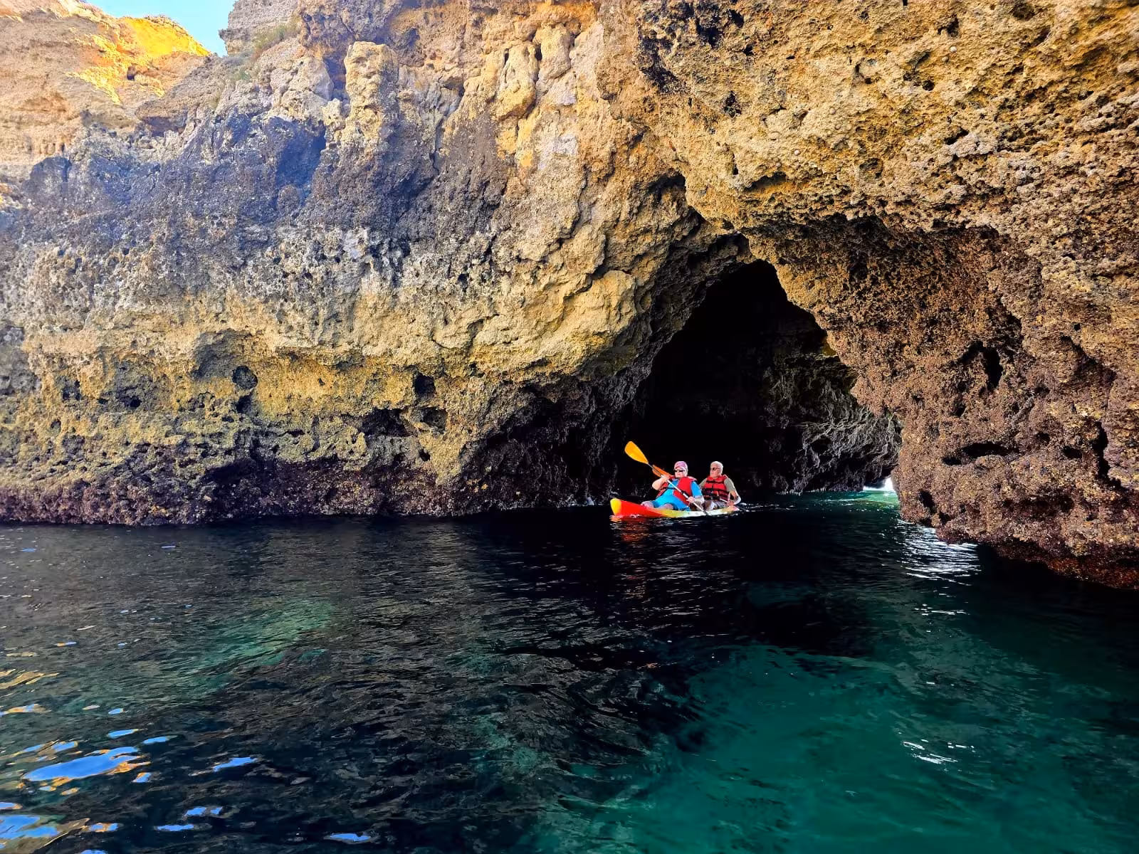 Two kayakers in life vests paddling out of a dramatic Albufeira sea cave on a private kayak tour