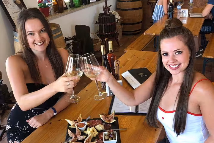 Two women enjoying wine and a charcuterie platter at an Algarve winery during a full-day tour from Albufeira.