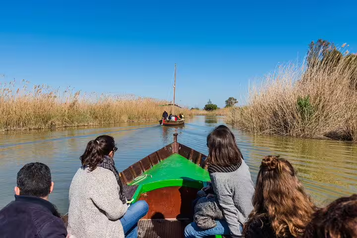 Tourists enjoy a tranquil boat ride through Albufera's serene waters during a private day trip featuring paella and nature trek.