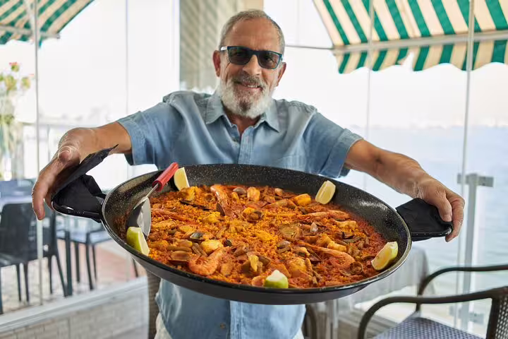 Man showcasing a large, freshly made seafood paella, part of the Private Albufera Day Trip featuring paella, boat ride, and nature trek.