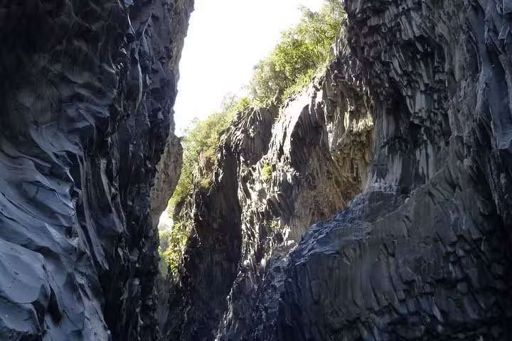 Dramatic basalt rock formations of Alcantara Gorge with lush greenery on the canyon walls.