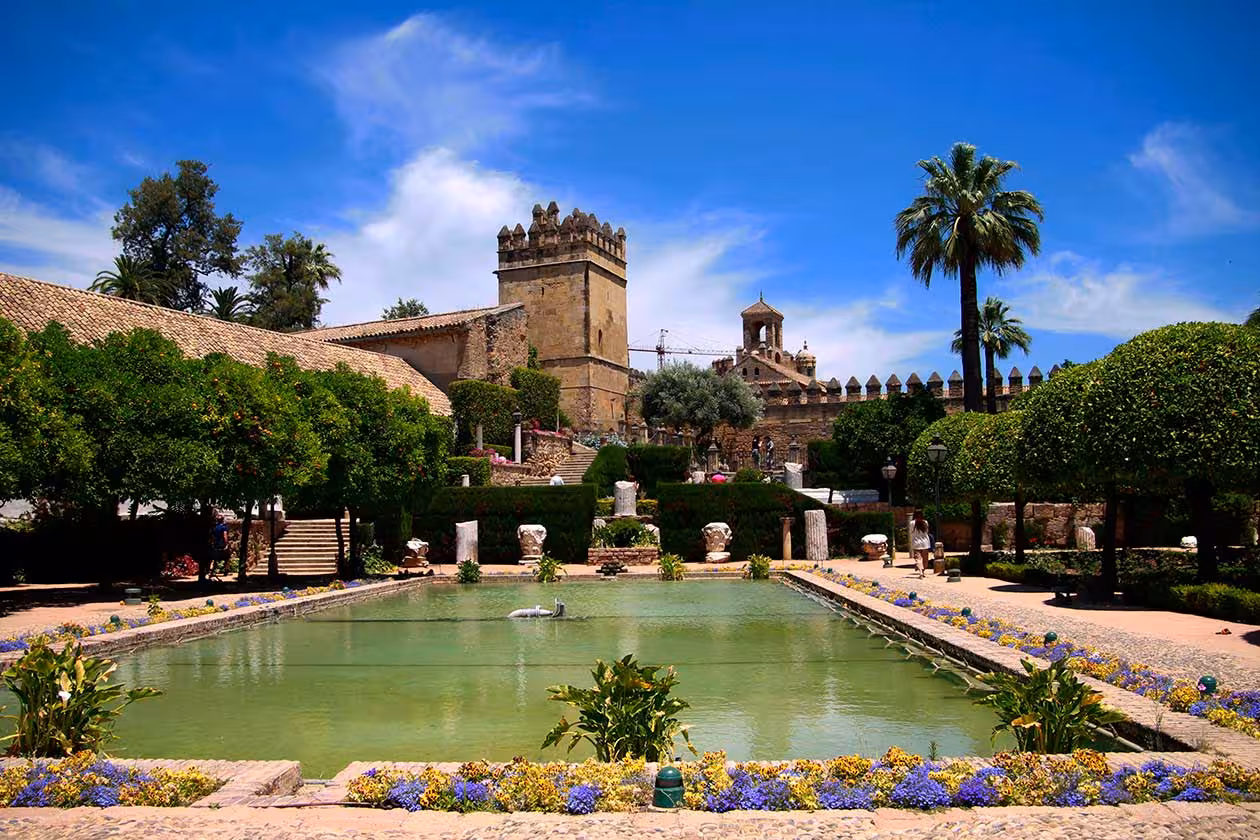 Scenic view of the Alcázar of the Christian Monarchs with a tranquil reflecting pool and lush gardens in Córdoba.