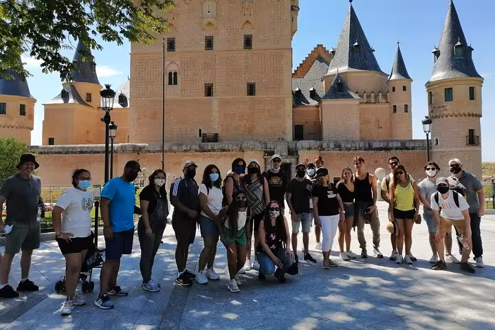 Group of tourists enjoying a sunny day in front of the majestic Alcazar of Segovia during a guided tour.