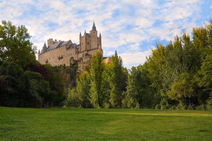 The majestic Alcázar of Segovia rises above verdant trees and a grassy field on a picturesque day trip from Madrid.