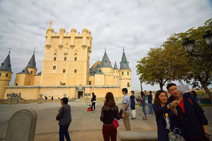 Tourists admire and take photos of the iconic Alcázar of Segovia on a sunny day during a half-day trip from Madrid.