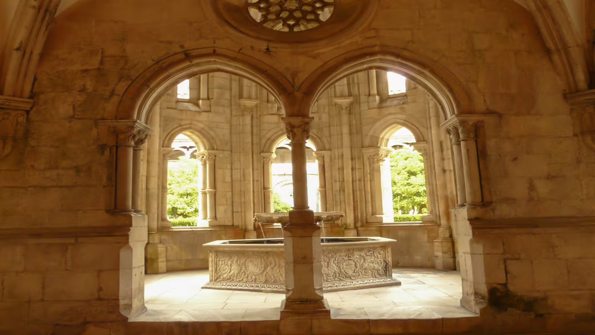 Interior view of Alcobaça Monastery's cloister with intricate stone arches and a carved fountain, part of the Nazaré and Alcobaça tour.
