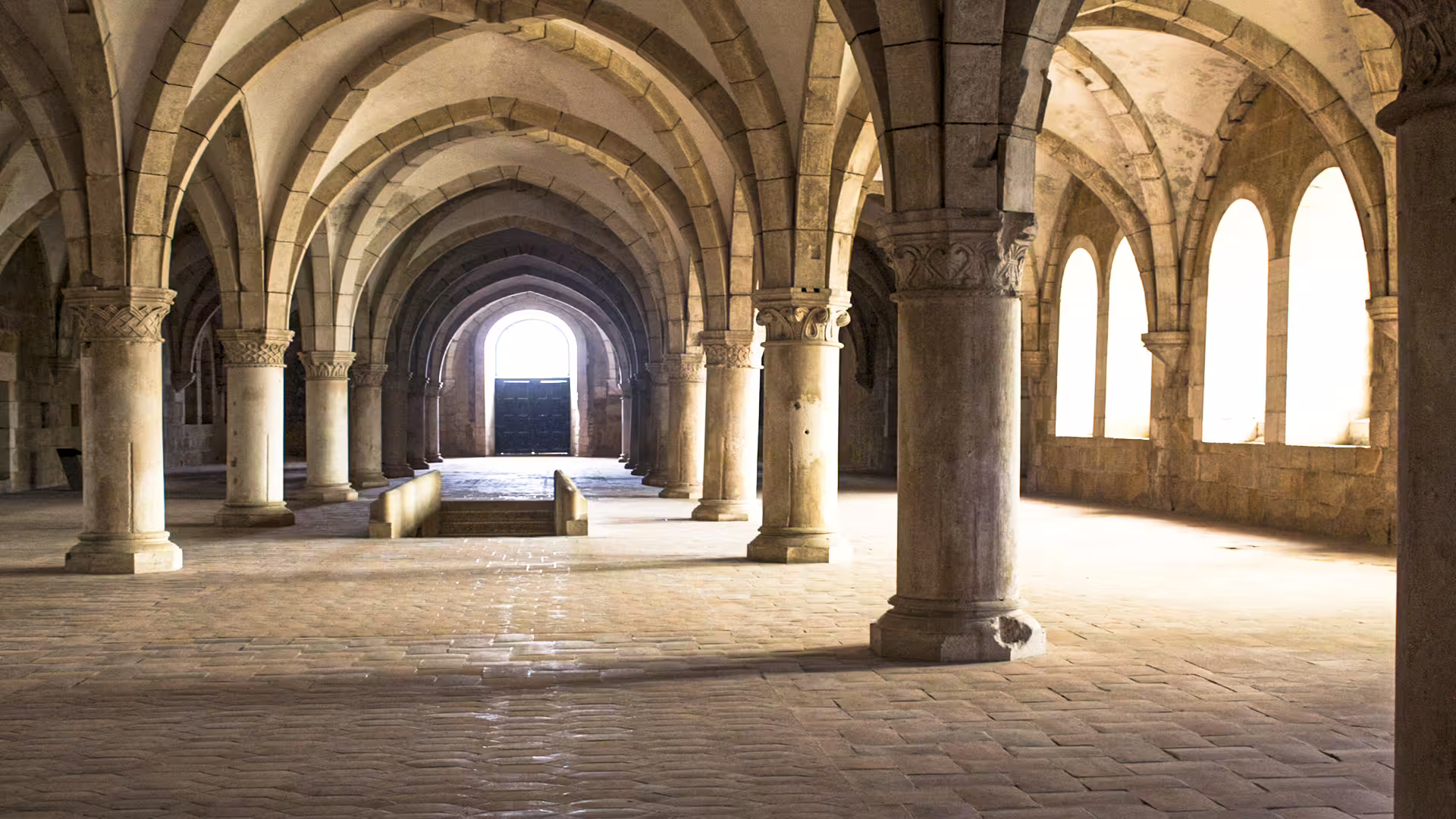 Sunlit arches of Alcobaça Monastery's cloister, showcasing stunning medieval architecture on a private Nazaré tour.