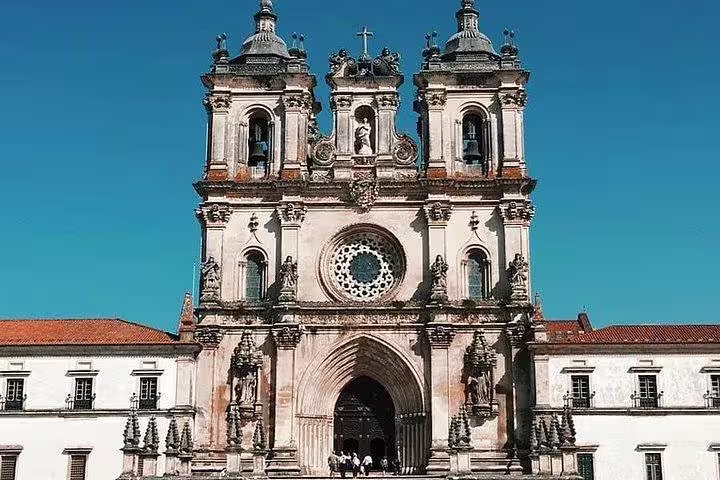 Majestic facade of the Alcobaça Monastery under clear blue skies in Portugal's Fátima and West coast tour.