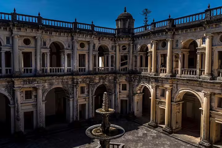 Historic courtyard with ornate arches and a central fountain in Alcobaça, showcasing Portuguese architecture under a clear blue sky.