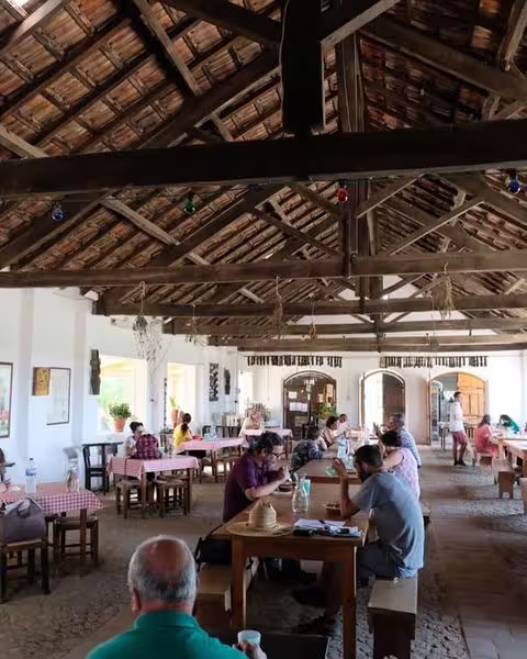 Rustic Alentejo dining room with guests enjoying a traditional meal under a wooden beamed ceiling.