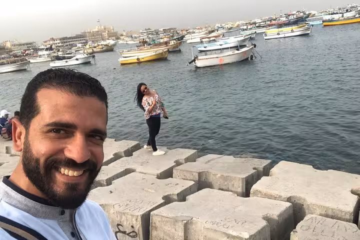 Travelers on Alexandria harbor breakwater with fishing boats, private guided day trip from Cairo Egypt