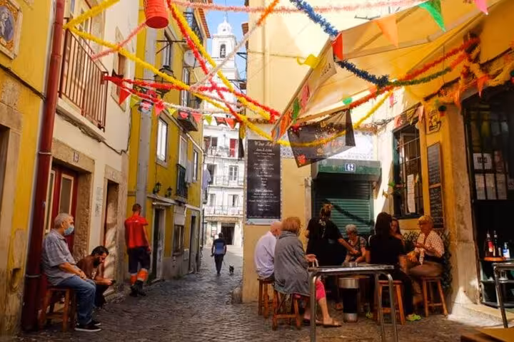 Colorful Alfama alley with café tables, perfect stop on a 4-hour private Tuk Tuk tour in Lisbon