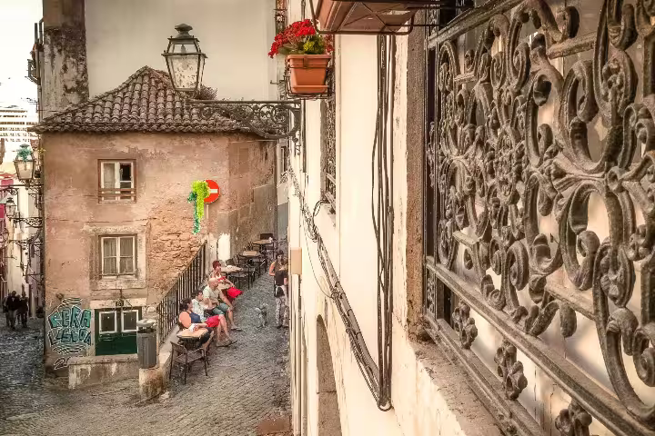 Charming Alfama street scene with ornate ironwork, cobblestone paths, and locals enjoying an outdoor café, ideal for photography.