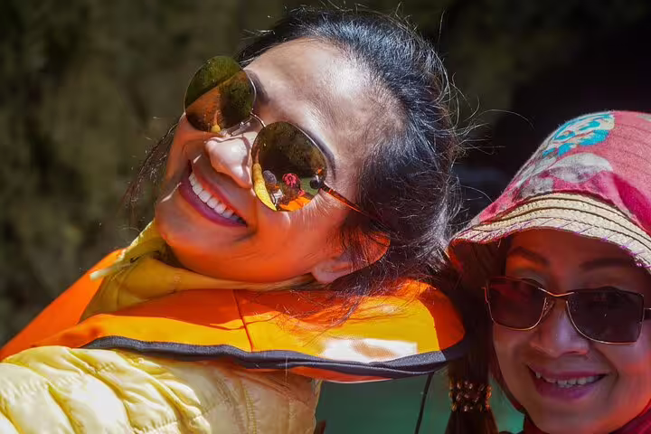 Two smiling women in sunglasses enjoy a sunny boat trip during the Algarve full-day private tour from Lisbon to Benagil caves.