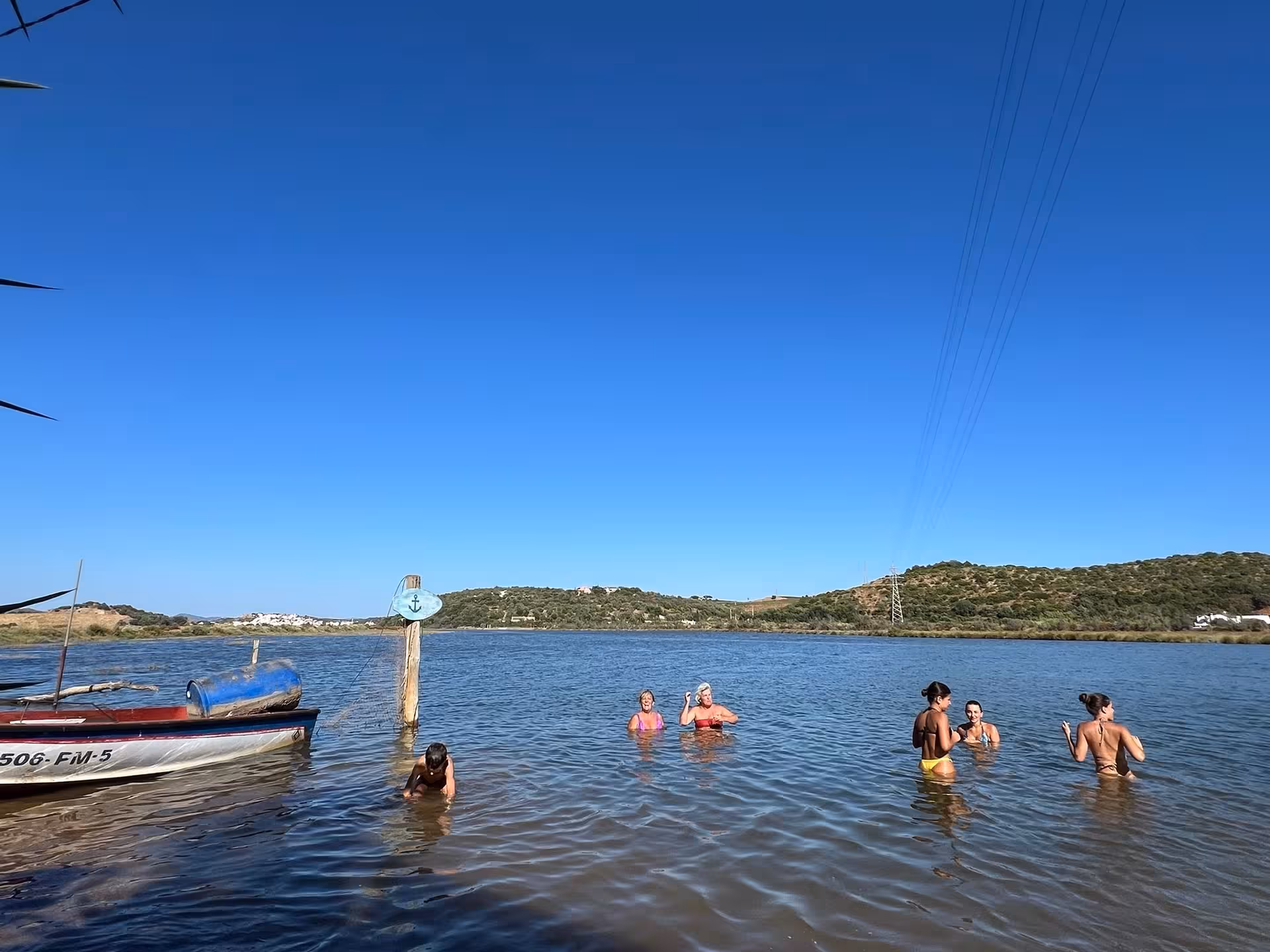 Friends relax and swim in shallow river waters beside a small charter boat on a sunny tailor‑made Algarve boat tour
