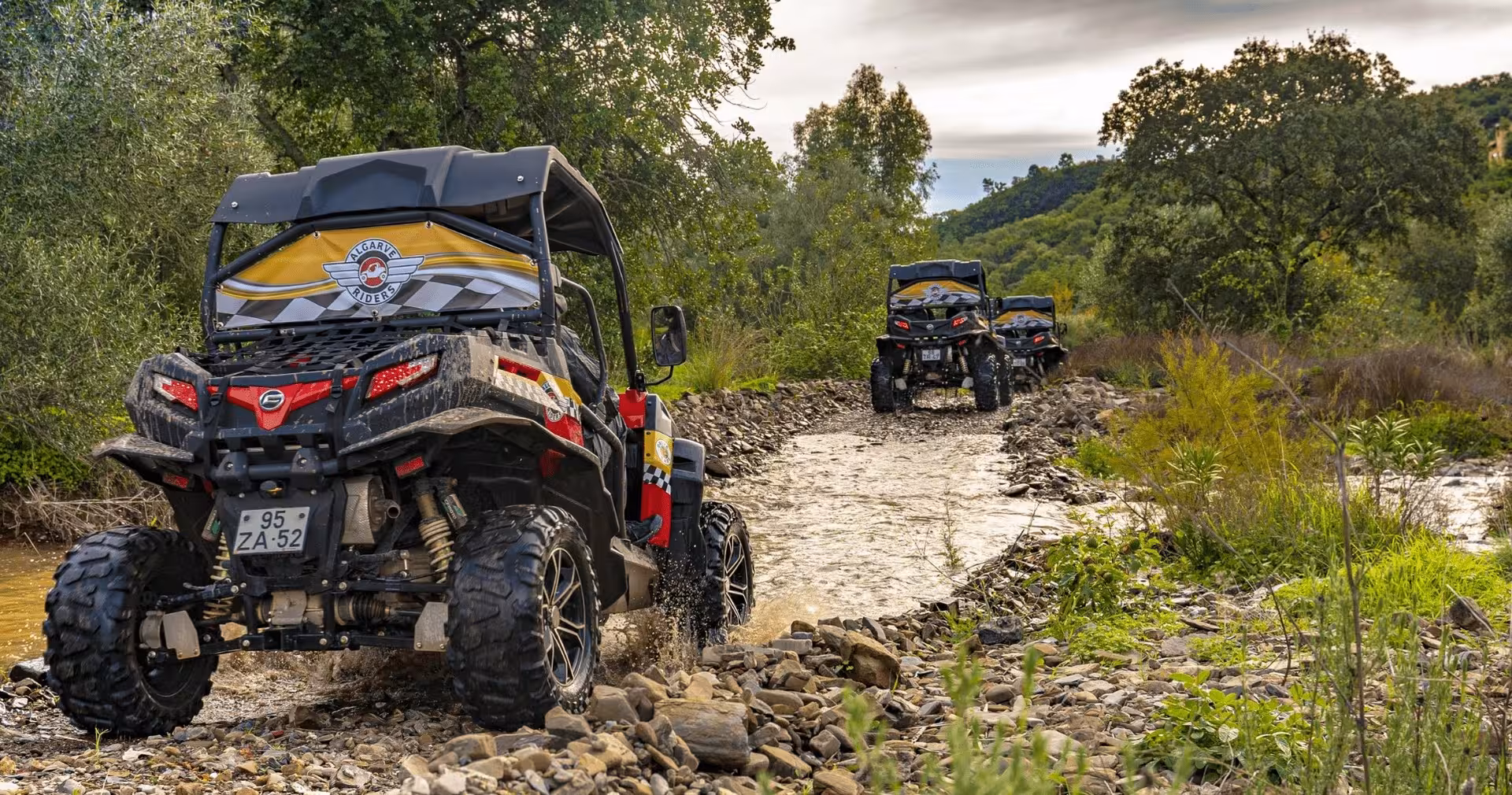 Off-road buggies driving through a rocky riverbed on a full day Algarve buggy tour surrounded by lush countryside scenery