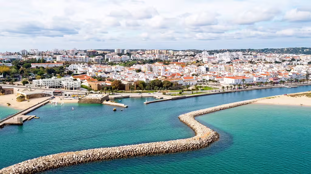 Aerial view of Algarve's coastal town with vibrant white buildings, clear blue waters, and a scenic promenade from Lisbon tour.