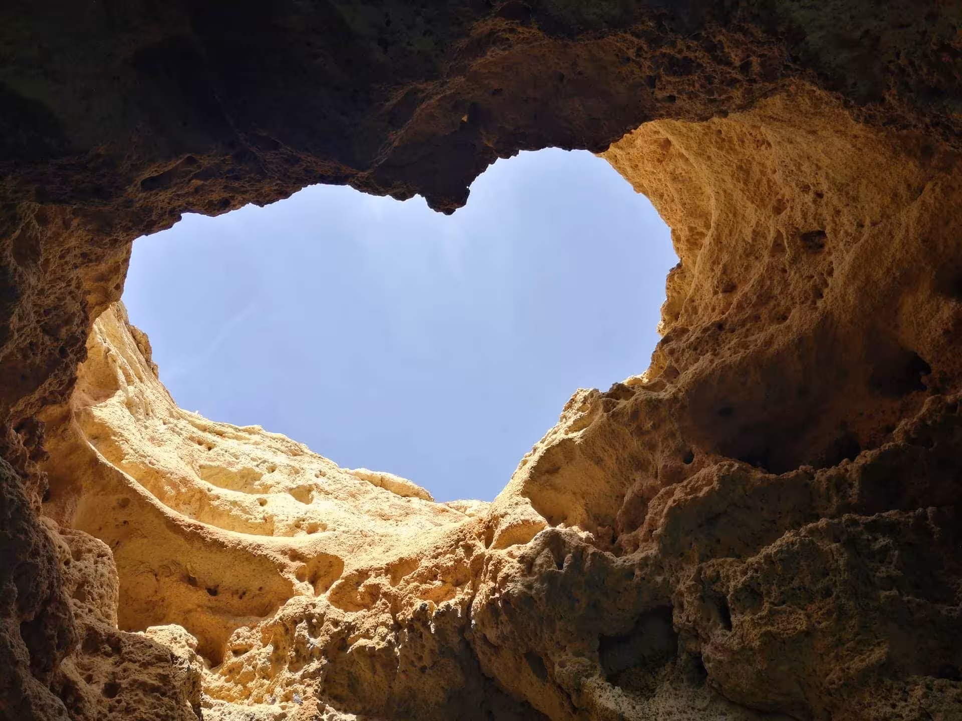View from inside Algarve heart-shaped sea cave ceiling framing bright blue sky on romantic coastal adventure