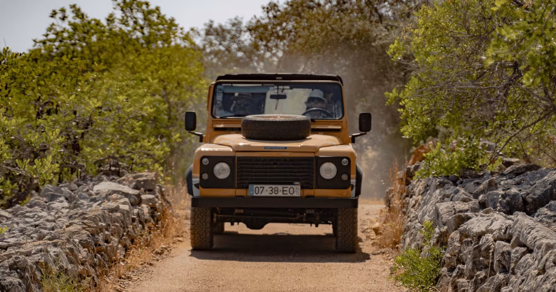 Vintage 4x4 jeep driving a dusty rural track between stone walls and green countryside on The Algarve Heritage Journey tour