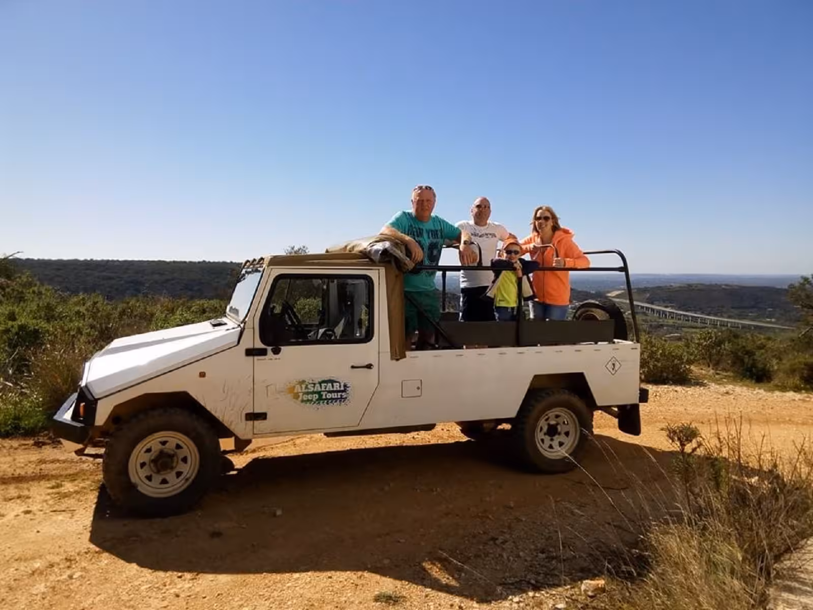 Family enjoying Algarve jeep safari tour in open 4x4, overlooking rugged hills and coastal sunset with sparkling wine