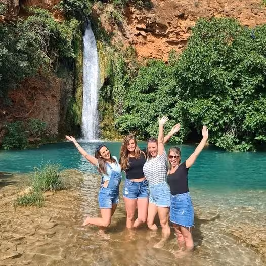 Group of friends posing in clear lagoon beneath Algarve waterfall, enjoying refreshing swim stop on full-day jeep safari