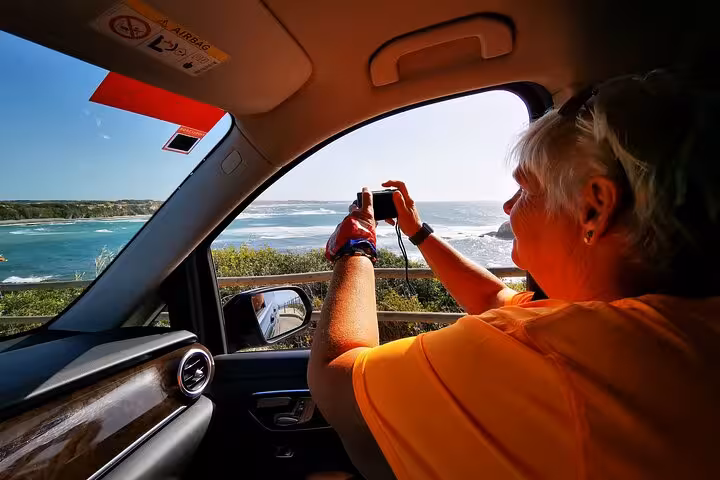 Passenger photographing Algarve coastline from private transfer car en route to Lisbon with scenic stop