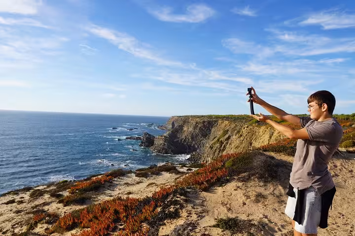 Traveler taking photos at Algarve sea cliffs viewpoint during private transfer from Algarve to Lisbon with stops