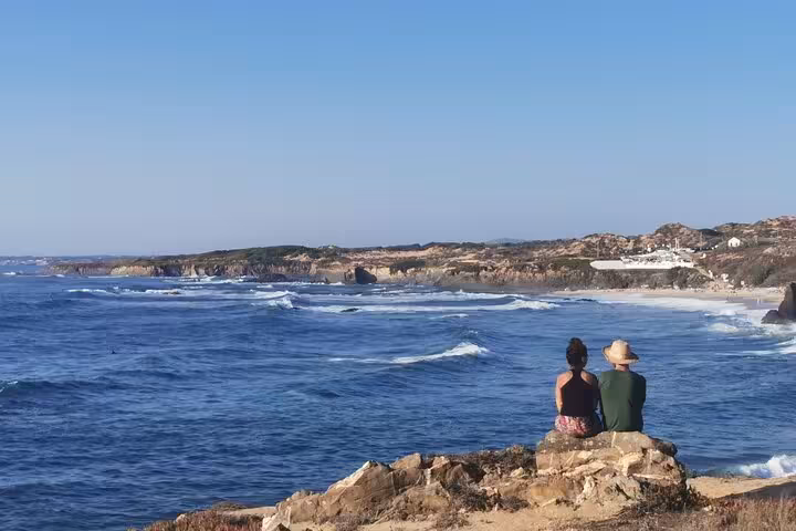Couple watching Atlantic waves on Algarve cliffs, scenic stop on private transfer from Algarve to Lisbon