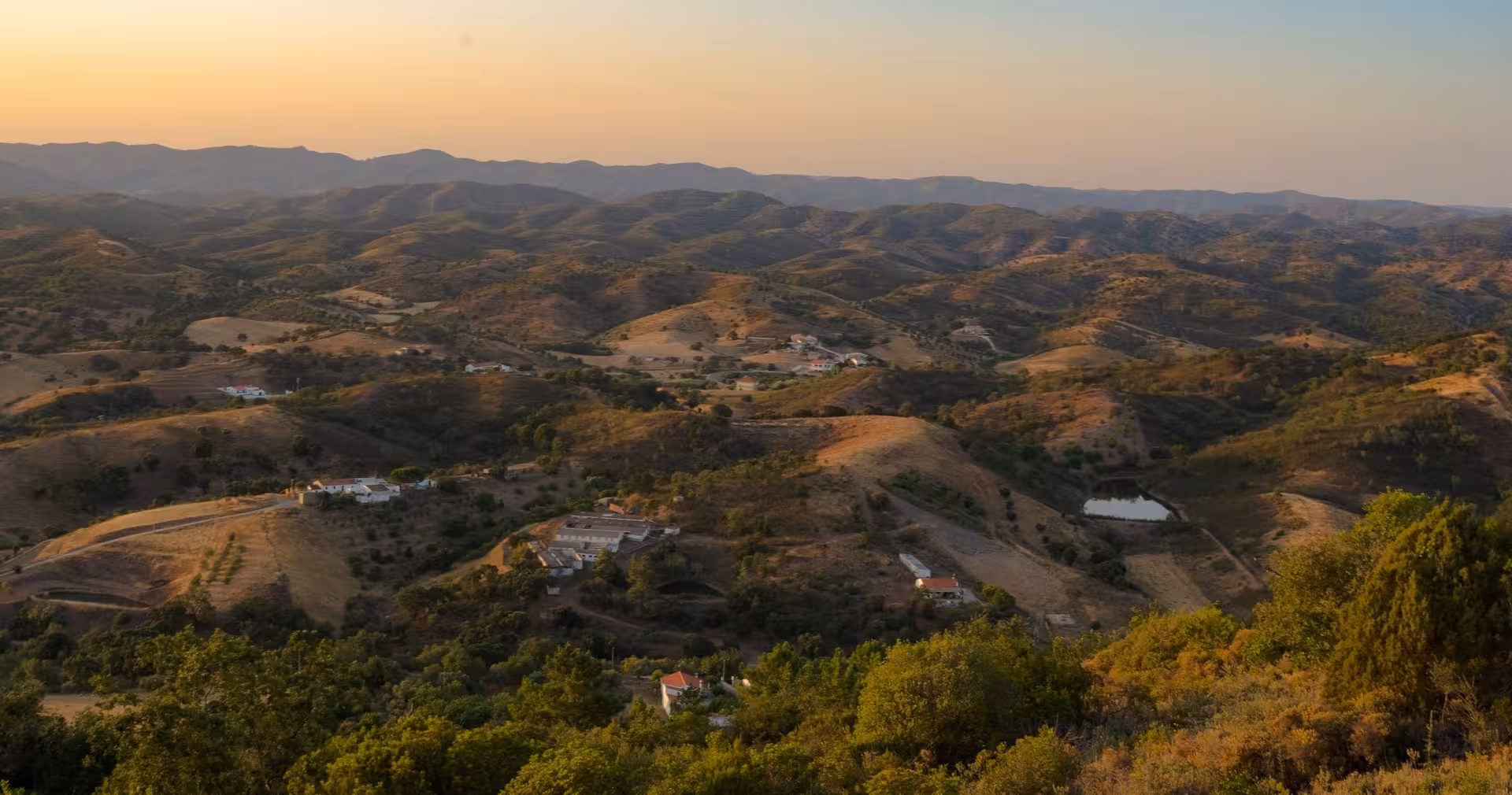 Golden sunset over rolling Algarve mountains with scattered farmhouses, forests and valleys on The Crafts & Mountains Journey