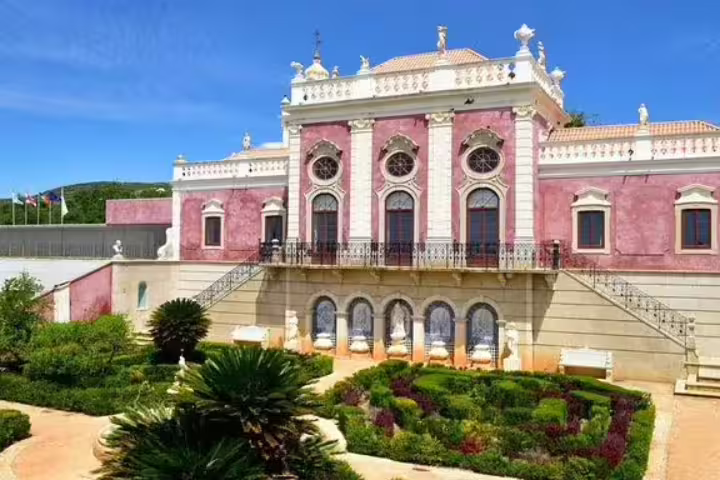 Elegant pink palace with ornate architecture and lush gardens under a clear blue sky, highlighting Algarve's cultural heritage.