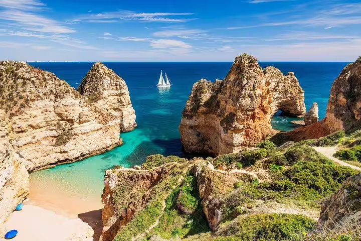 Stunning Algarve coastline with dramatic cliffs, turquoise waters, sandy beach, and a sailboat; perfect for private tours.