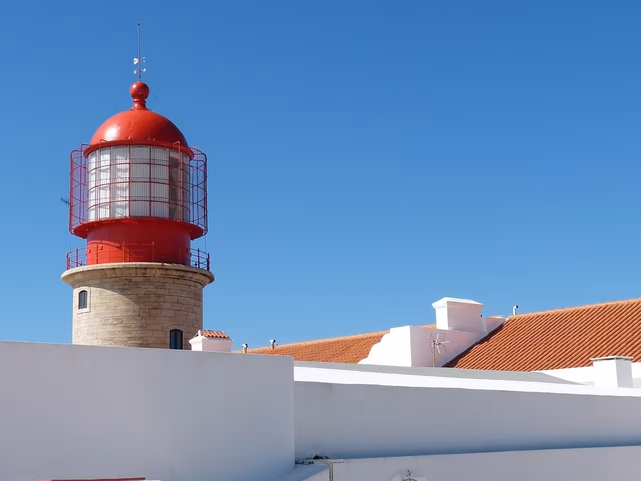 Red lighthouse and whitewashed buildings under clear blue sky on Algarve à la Carte coastal sightseeing tour, Portugal