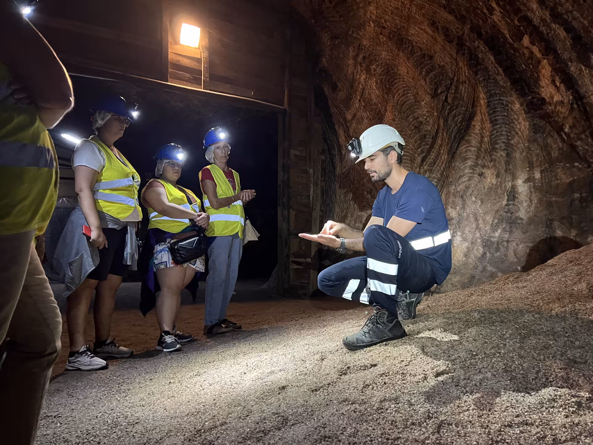 Guide explains rock formations to tourists in Loulé rocksalt mine during Algarve tour, wearing helmets and vests.
