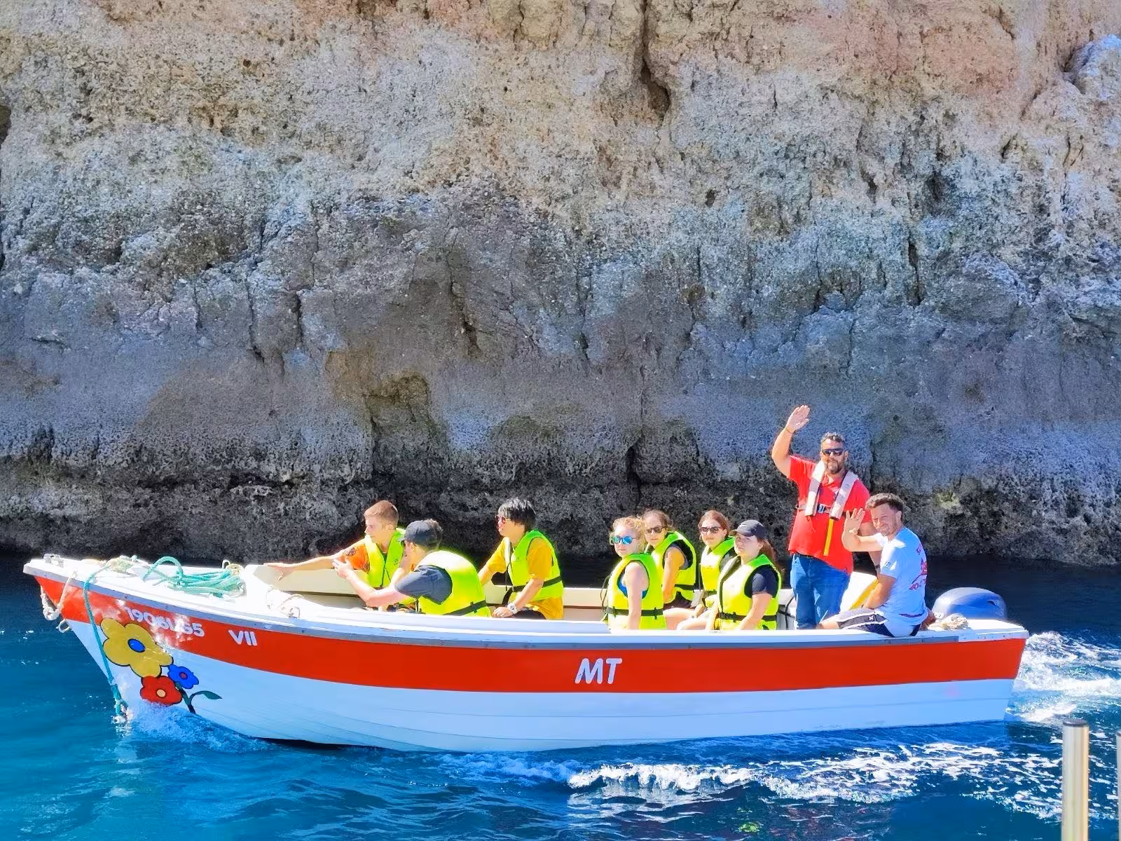 Small guided boat with tourists in life jackets explores coastal caves on a 2-hour Algarve sailing and grotto tour