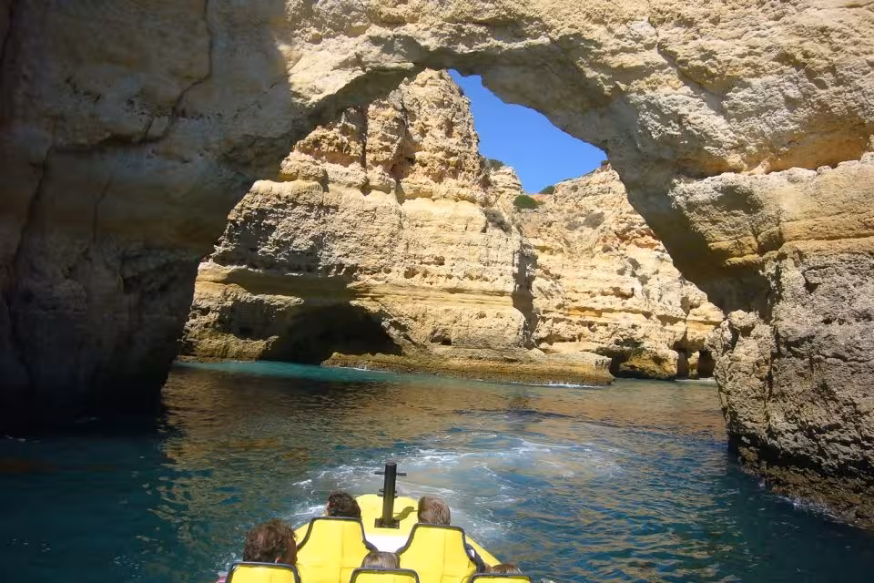 Tourists on a boat explore stunning Algarve sea caves with natural rock arches and clear blue waters.