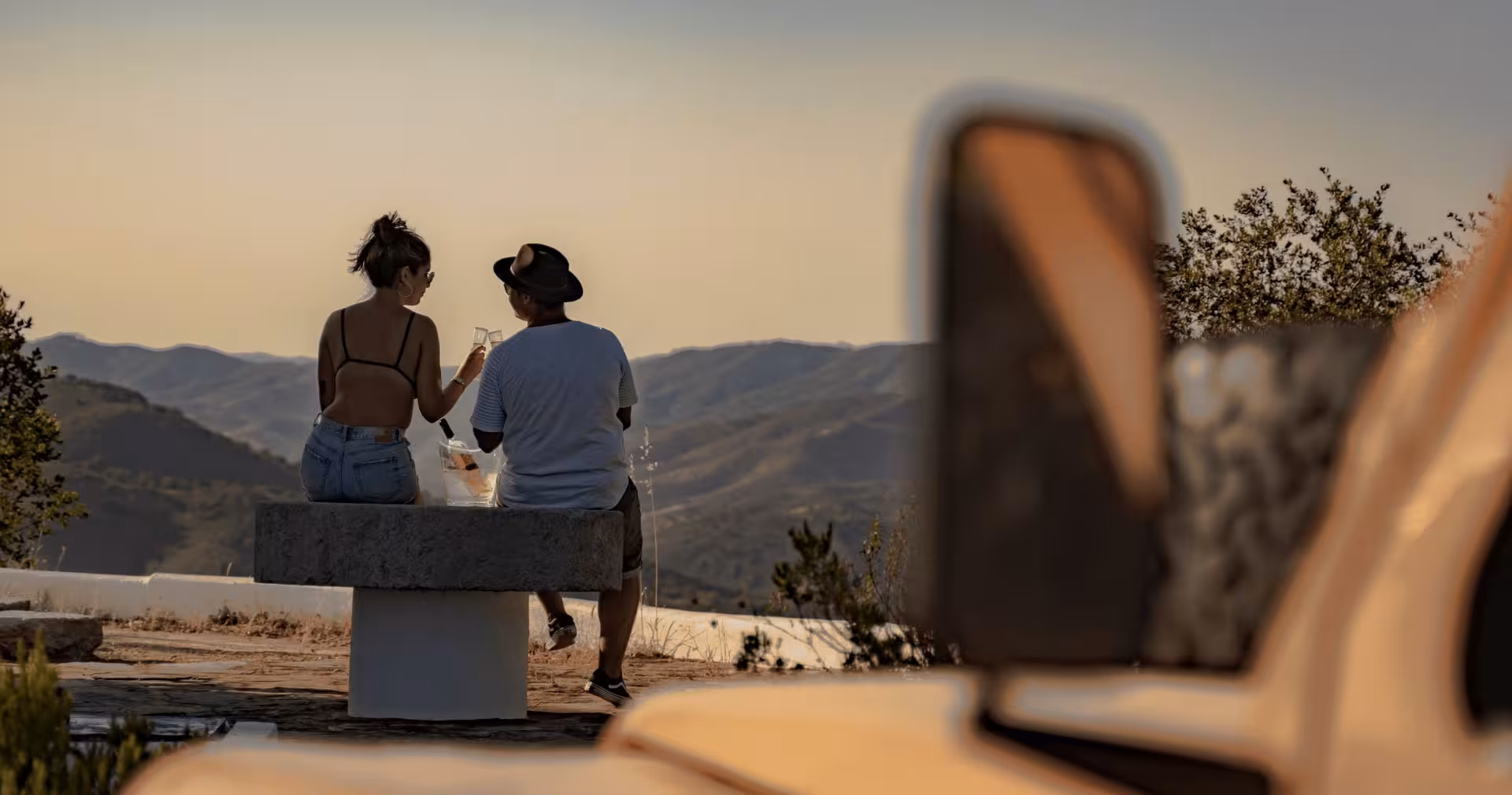 Couple toasting with champagne on a hilltop bench overlooking Algarve mountains at golden sunset