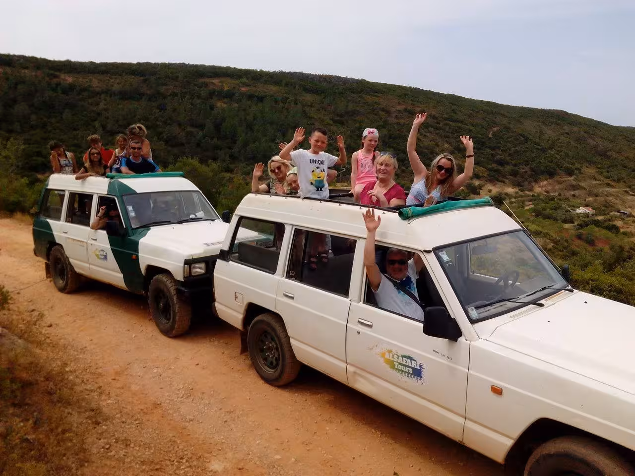 Happy travelers on 4x4 jeeps wave during an Algarve countryside sunset safari tour, combining off-road adventure with sparkling wine