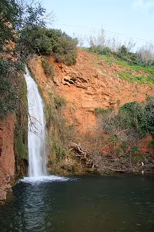 Hidden Algarve waterfall cascading down red cliffs into a tranquil pool, a scenic stop on the Sunset Jeep Safari tour