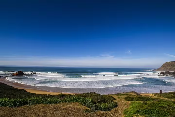Pristine Algarve west coast beach with rolling waves and lush greenery, ideal for nature exploration and relaxation.