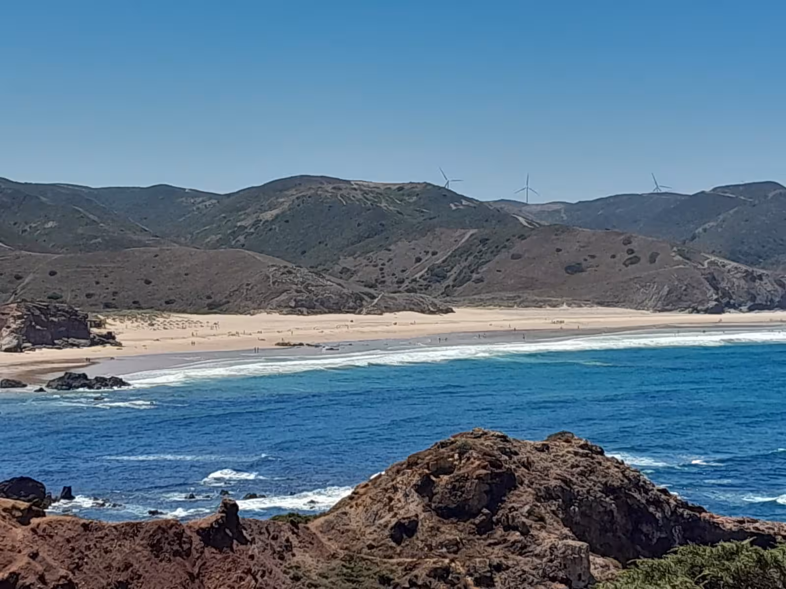 Golden sandy beach, turquoise surf and rolling green hills with wind turbines on an Algarve West Coast day tour