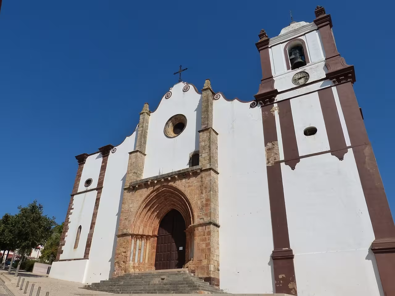 Historic white church with stone portal and bell tower under clear blue sky on Algarve à la Carte cultural tour in Portugal