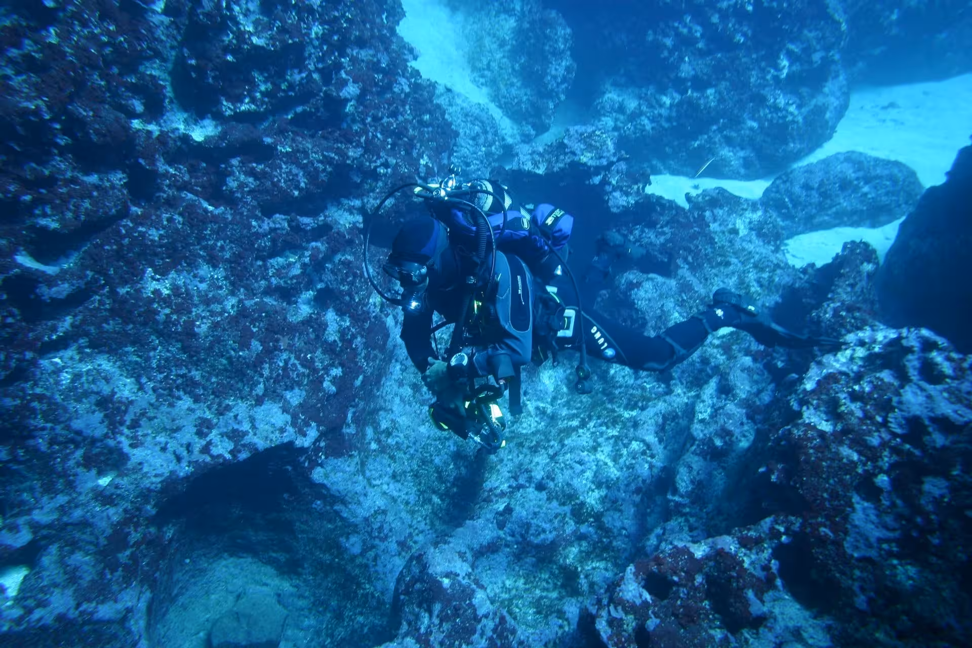 Diver exploring rocky underwater terrain in Alghero during beginner discovery lesson.