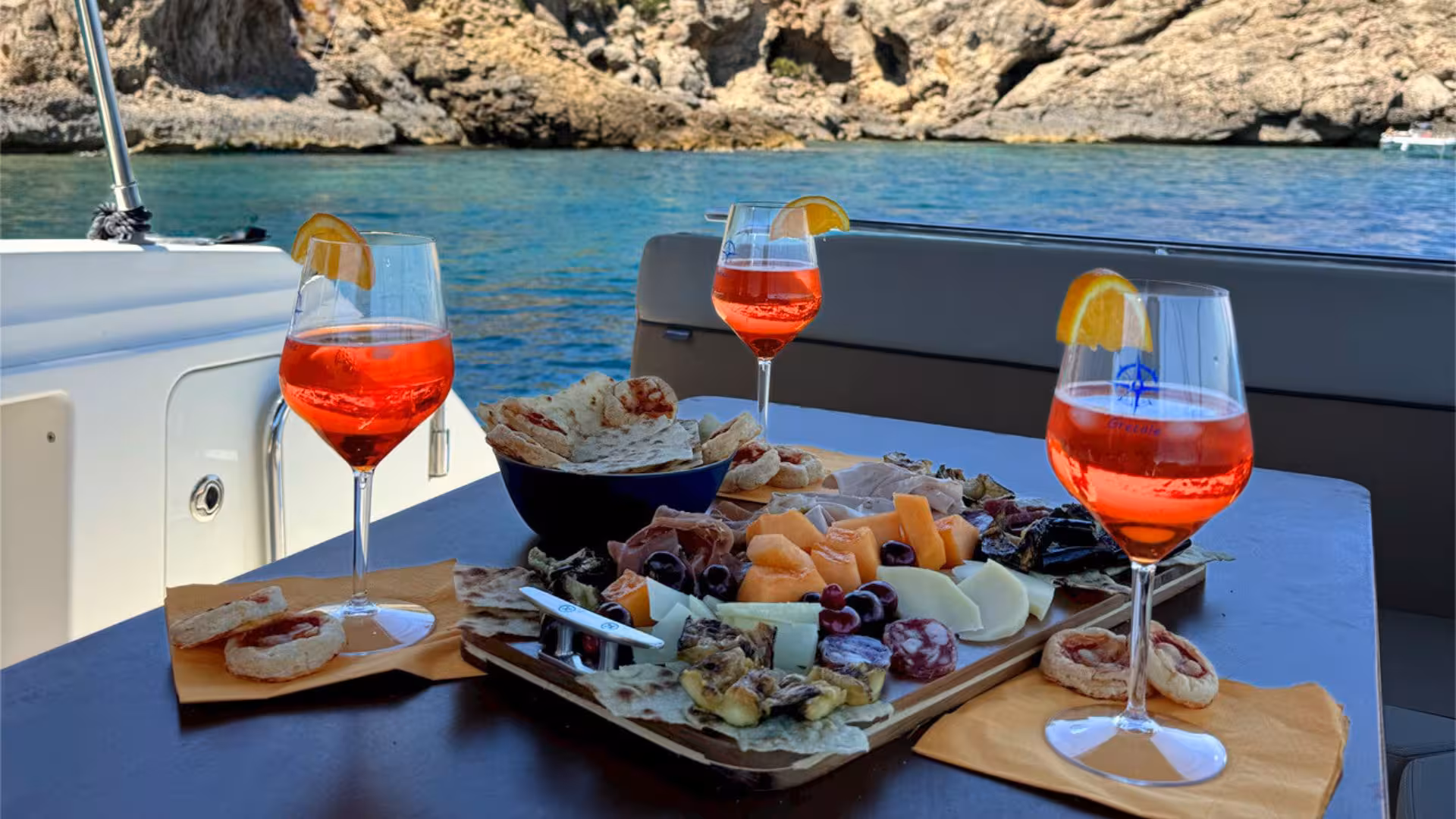 Exquisite Mediterranean snacks and Aperol spritz on a scenic boat ride from Alghero, showcasing stunning coastal views.