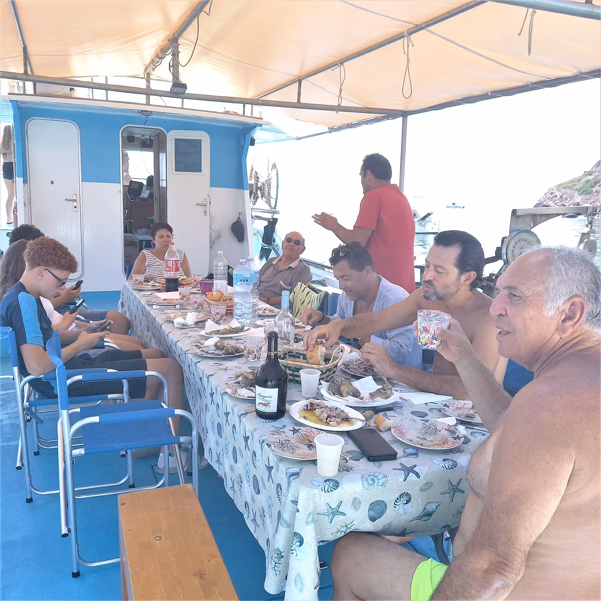 Group enjoying a hearty seafood meal on a boat during Alghero's Capo Caccia fishing tour.