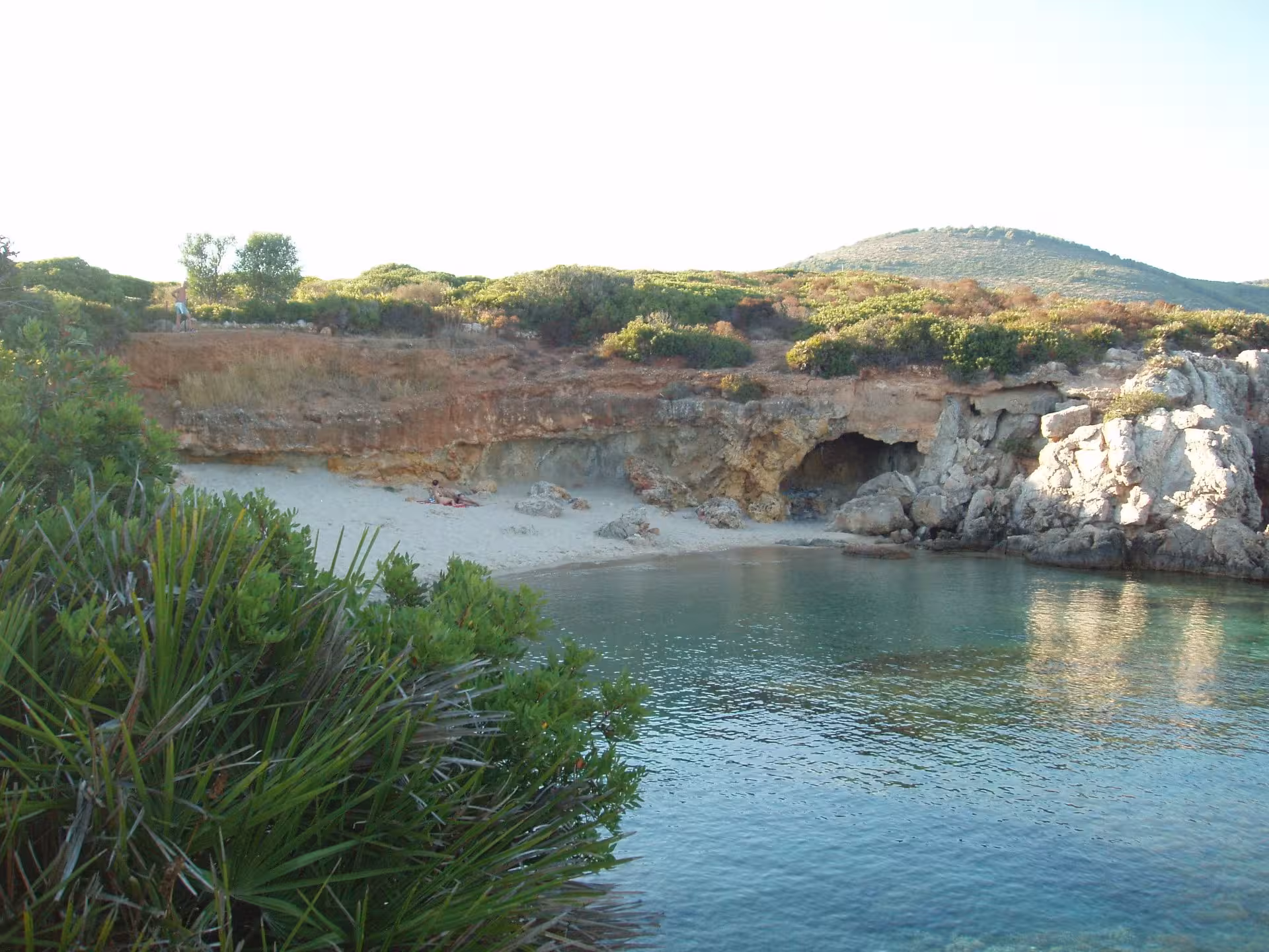 Hidden cove with crystal clear waters and rocky cliffs along the Alghero coastline, ideal for e-bike tours.