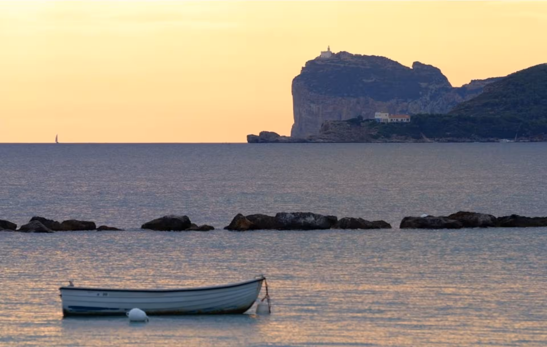 Serene sunset over the Alghero coastline with a solitary boat and distant cliffs in the background.